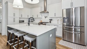 A modern kitchen with white cabinetry, a stainless steel refrigerator, a central island with bar stools, and pendant lighting. - Private Hot Tub| Community Pool| Boat Docks| Perdido Beaches| Yard Games| Close to NAS| Free Golf (Pensacola)