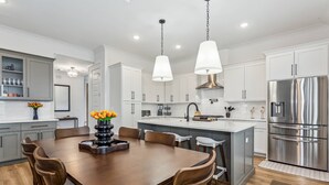 A modern kitchen with white cabinets, stainless steel appliances, and a wooden dining table with chairs. - Private Hot Tub| Community Pool| Boat Docks| Perdido Beaches| Yard Games| Close to NAS| Free Golf (Pensacola)