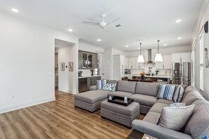 A modern living room with a sectional sofa, ottoman, and a dining area with pendant lights. - Private Hot Tub| Community Pool| Boat Docks| Perdido Beaches| Yard Games| Close to NAS| Free Golf (Pensacola)