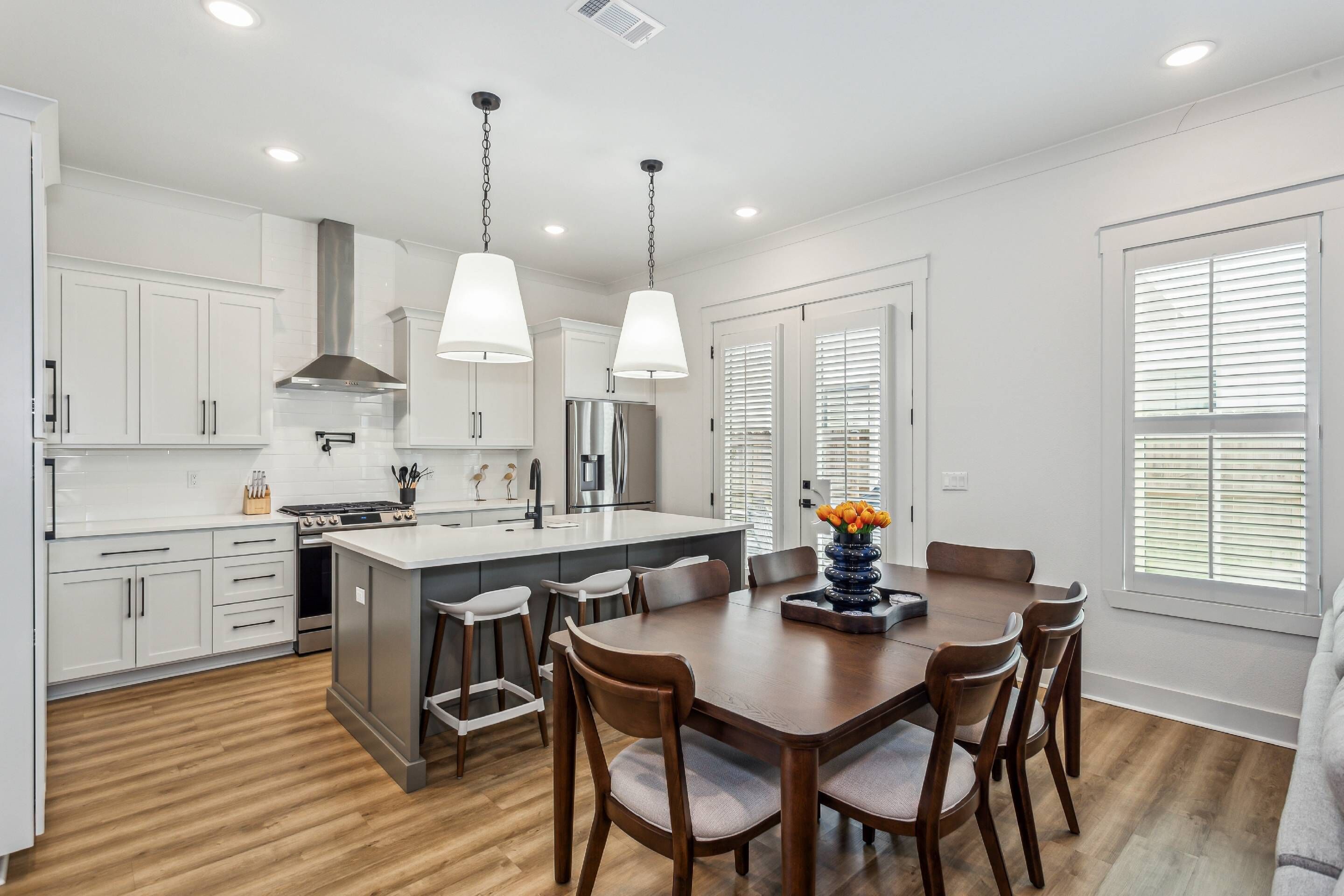 A modern kitchen with white cabinets, stainless steel appliances, and a wooden dining table with chairs.