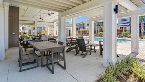 An outdoor patio area with tables and chairs, a ceiling fan, and a view of a swimming pool and neighboring houses. - Private Hot Tub| Community Pool| Boat Docks| Perdido Beaches| Yard Games| Close to NAS| Free Golf (Pensacola)