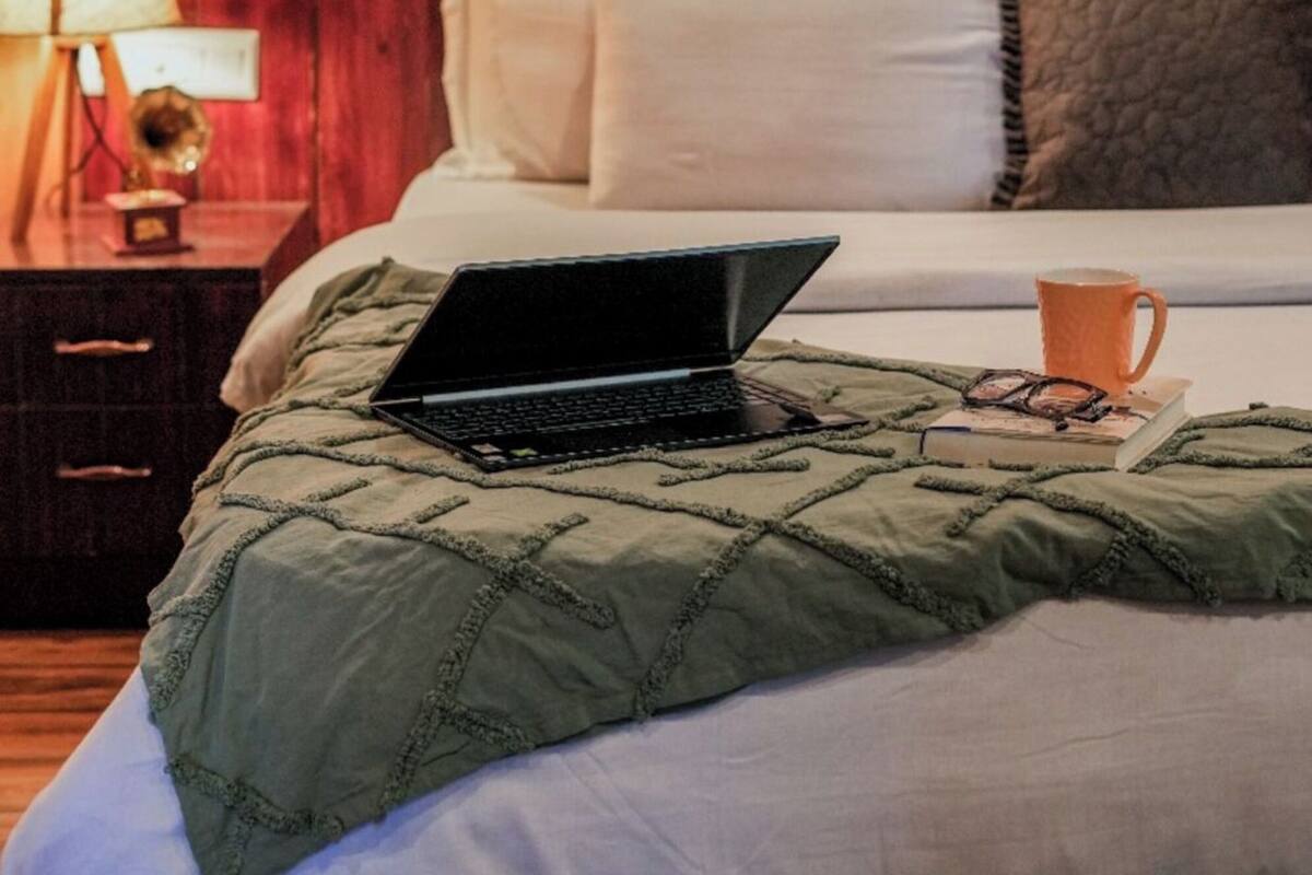 A hotel room with a bed, a laptop, a coffee cup, and a painting on the wall.