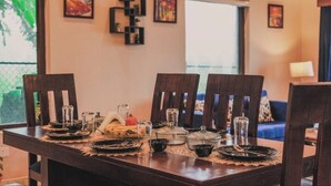 Una mesa de comedor dispuesta con platos, vasos y un centro de mesa de calabaza, rodeada de sillas en una habitación con obras de arte en las paredes.