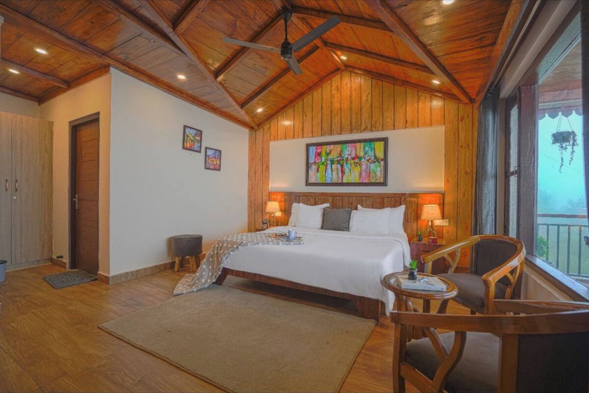A spacious bedroom with a large bed, wooden ceiling, and a balcony with a view.