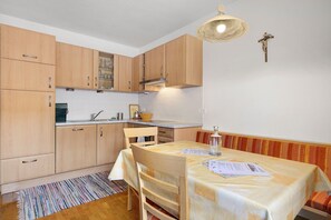 Une petite cuisine avec des meubles en bois, une table à manger couverte de papiers et un symbole religieux accroché au mur.