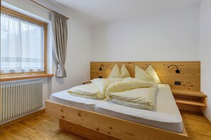 Une chambre à coucher avec un lit en bois, une fenêtre avec des rideaux, une table de chevet et une lampe fixée au mur.