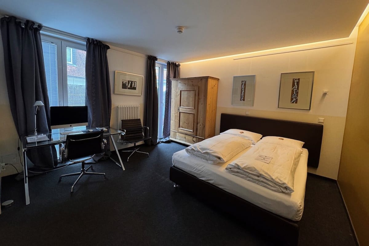 Una habitación de hotel con cama, escritorio, silla, computadora y obras de arte en las paredes.