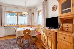 A room with a wooden dining table, a TV on a wooden cabinet, and a window with curtains. - Apartment 'Goller Saslonch' with Mountain View, Balcony and Wi-Fi (ORTISEI)