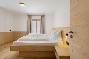 A bedroom with a wooden bed frame, a window with curtains, and a wall-mounted light fixture. - Apartment 'Goller Saslonch' with Mountain View, Balcony and Wi-Fi (ORTISEI)