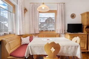 A cozy room with a wooden bench, a table with a white tablecloth, a television, and a window with curtains. - Apartment 'Goller Saslonch' with Mountain View, Balcony and Wi-Fi (ORTISEI)