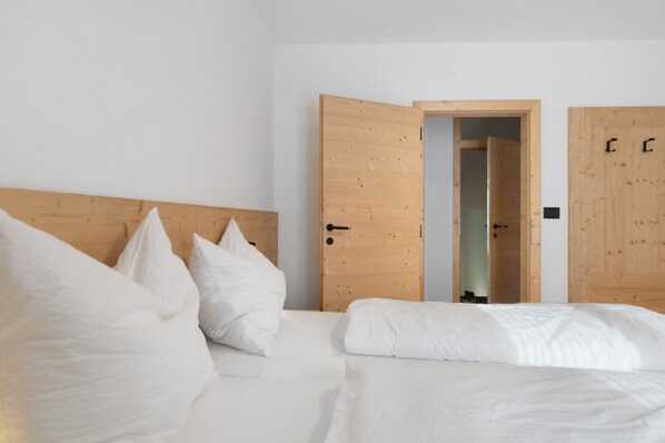 A bedroom with a wooden headboard, a bed with white bedding, and two open wooden doors leading to another room.