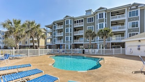 A pool area with blue lounge chairs and a pool, surrounded by a building with balconies and palm trees. - Myrtle Beach Condo w/ Pool Access, 2 Mi to Ocean! (Myrtle Beach)