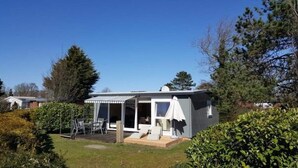 A small, single-story house with a patio area, a covered outdoor seating area, and a lawn. - Pretty Bungalow in Sint Maartenszee (Sint Maartensvlotbrug)