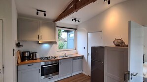 A compact kitchen with modern appliances, a window, and a small dining area with a white table and bench. - Pretty Bungalow in Sint Maartenszee (Sint Maartensvlotbrug)