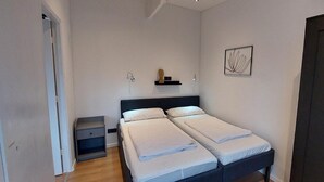 A bedroom with two beds, a wardrobe, a bedside table, and a wall-mounted shelf with a decorative item. - Pretty Bungalow in Sint Maartenszee (Sint Maartensvlotbrug)