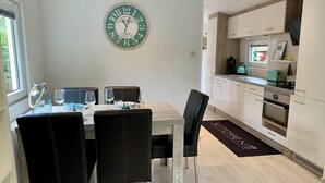 A modern kitchen with white cabinets, a black countertop, and a clock on the wall. - Furnished Chalet in Sint Maartenszee (Sint Maartensvlotbrug)