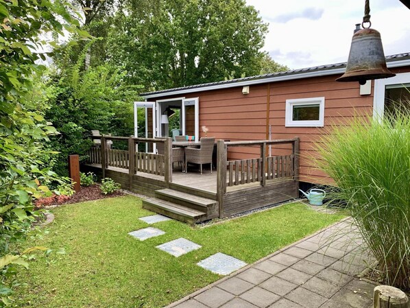 A wooden deck with outdoor furniture, a small garden with stepping stones, and a bell. - Furnished Chalet in Sint Maartenszee (Sint Maartensvlotbrug)