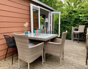 An outdoor patio with a glass table and wicker chairs, a lamp, and a chair with a cushion. - Furnished Chalet in Sint Maartenszee (Sint Maartensvlotbrug)