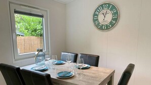 A dining table set with plates, glasses, and cutlery, surrounded by leather chairs. A large clock is mounted on the wall above the table. - Furnished Chalet in Sint Maartenszee (Sint Maartensvlotbrug)