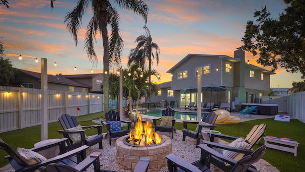 A backyard with a fire pit surrounded by Adirondack chairs, a pool, and a house with a white fence. - 4 Minutes to Beach | Pool | Hot Tub | Game Room (Seminole)