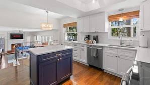 A modern kitchen with white cabinets, a central island, and a dining area with a fireplace. - 4 Minutes to Beach | Pool | Hot Tub | Game Room (Seminole)