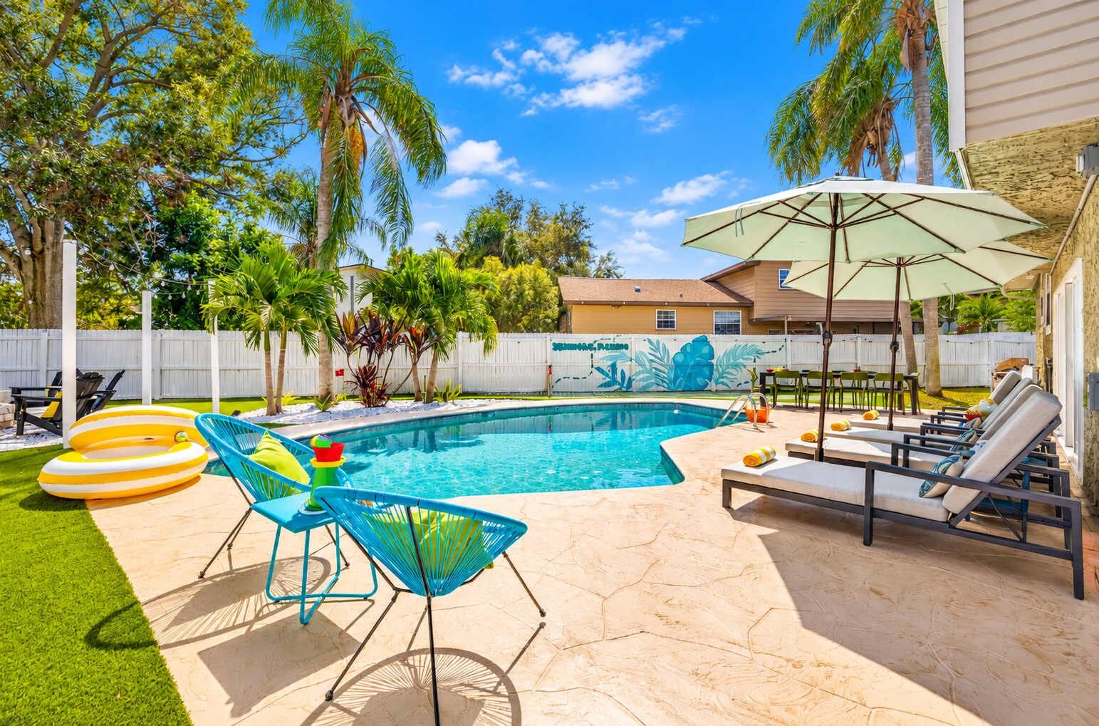 A backyard with a swimming pool, lounge chairs, and inflatable rings.