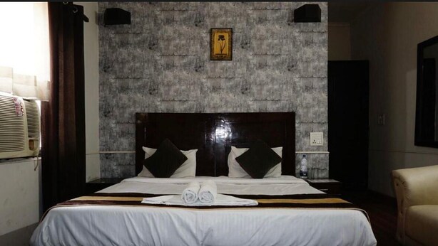 A hotel room with a large bed, a headboard, a wall-mounted picture, and a bedside table with a water bottle. - hotel ashi  (Satna)