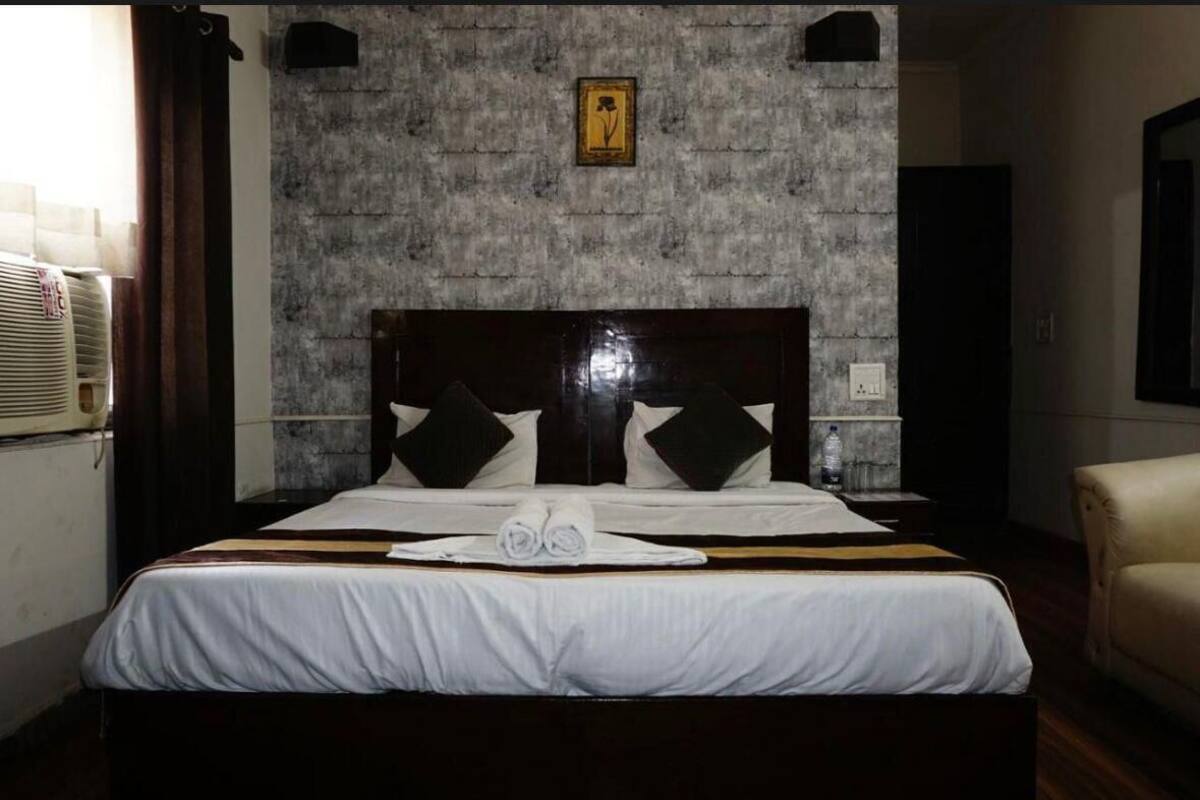 Habitación de hotel con una cama grande, cabecera, un cuadro colgado en la pared y una mesita de noche con una botella de agua.