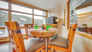 A dining area with a round wooden table, four wooden chairs with cushioned seats, and a view of snowy mountains through large windows.