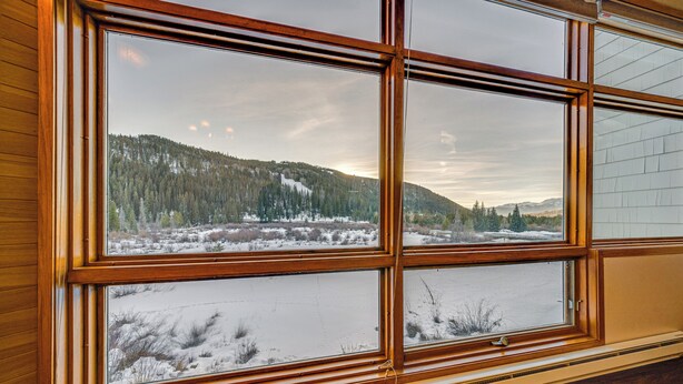 A room with large windows offering a view of a snowy landscape and forested hills.