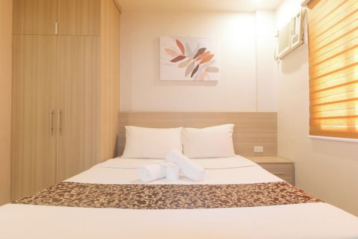 A hotel room with a bed, a wardrobe, a nightstand, and a wall-mounted air conditioner.
