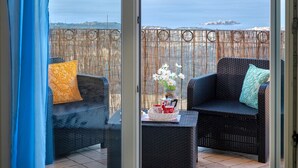A balcony with wicker furniture, a table with a vase of flowers, and a view of the sea.