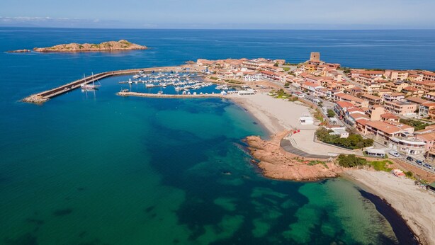 An aerial view of a coastal town with a marina, buildings, and a prominent tower.