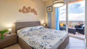 A bedroom with a bed, bedside table, lamp, and a view of the balcony.