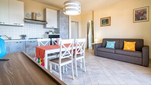 A modern kitchen with white cabinets, a dining table with chairs, a gray sofa, and a hanging light fixture.