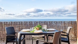 An outdoor dining area with a table set for two, chairs, and a view of the ocean.