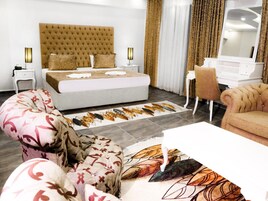 Una habitación de hotel moderna con una cama grande, un área de descanso con sofá y sillón, un escritorio y un espejo amplio.