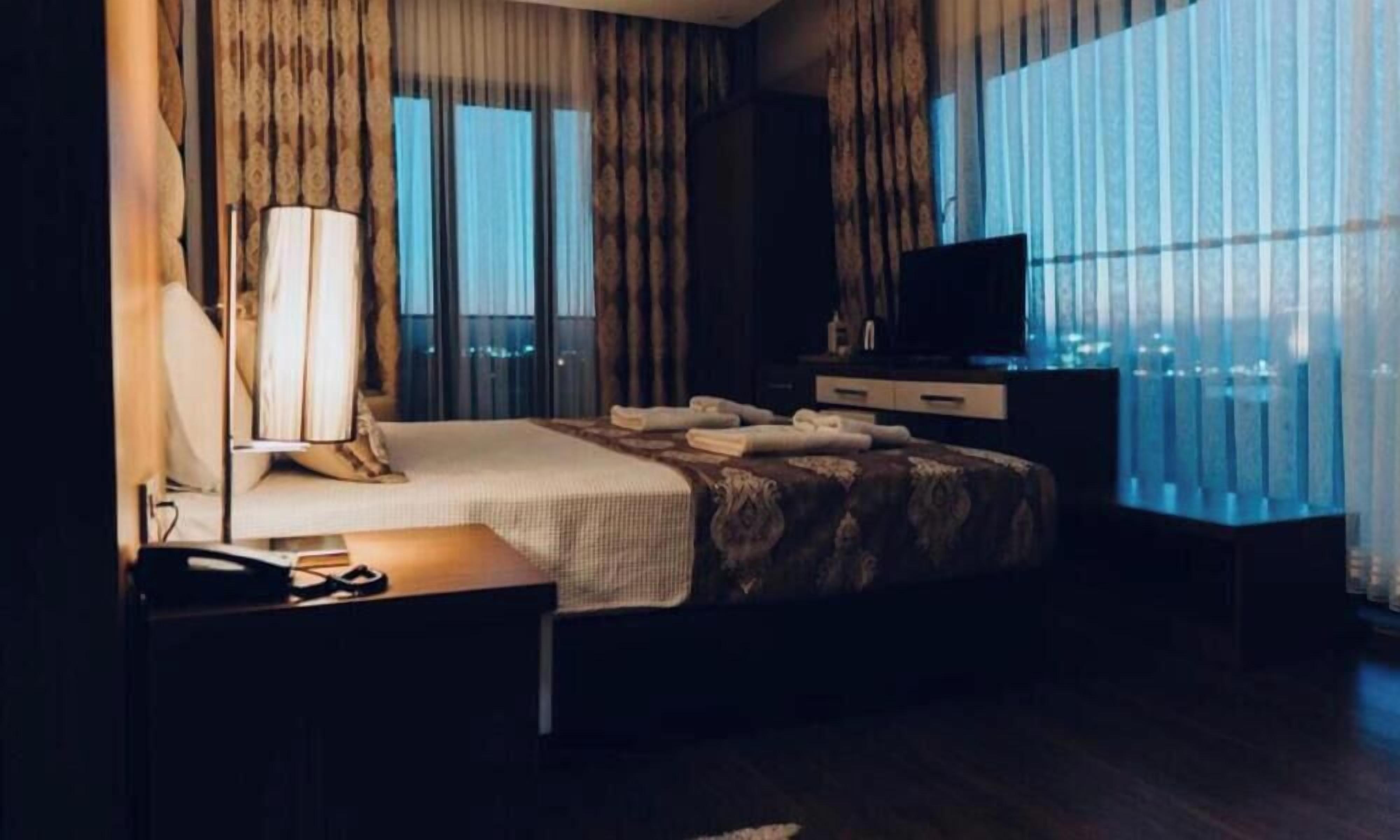 Una habitación de hotel con cama, escritorio, televisión y ventana con cortinas.