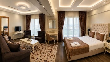Habitación de hotel con cama, escritorio, silla, sofá, televisor y espejo.