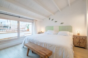 Une chambre avec un grand lit, un banc en bois, une table de chevet avec une lampe et une vue sur l’extérieur.