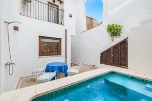 Un petit espace extérieur avec une piscine, une table et des chaises, une douche et une plante en pot.