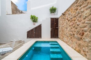 A swimming pool with a stone wall and wooden shutters, a white wall with a window, and a potted plant. - Holiday Home 'La Roca' with Mountain View, Wi-Fi and Air Conditioning (Pollença)