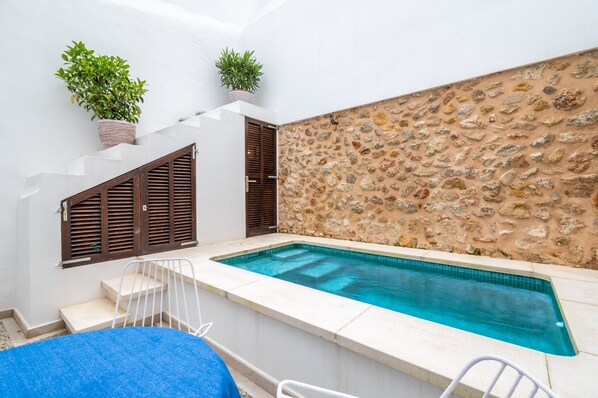 Une piscine aux murs en pierre, un escalier avec des volets en bois et des plantes en pot.
