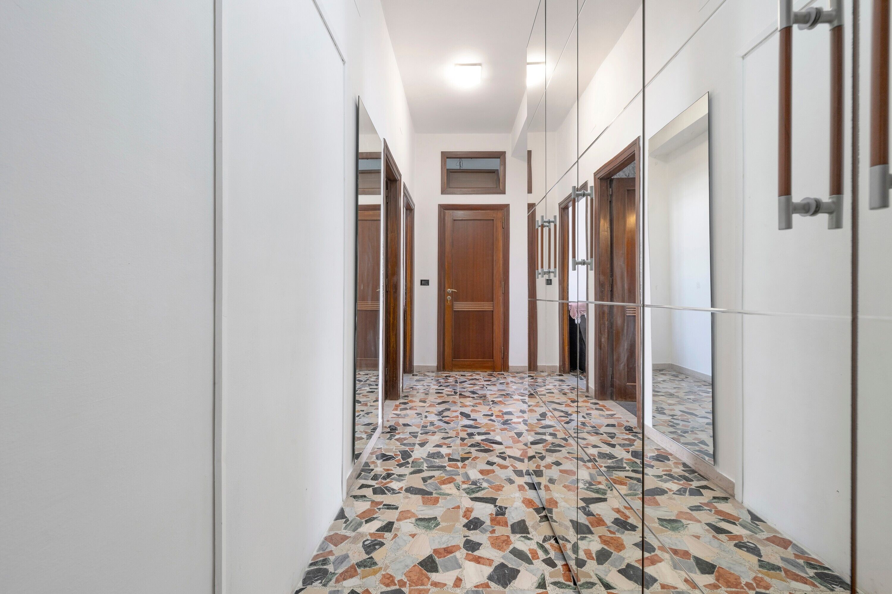 A hallway with a tiled floor, wooden doors, and a mirror on the wall.