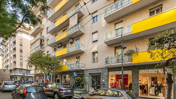 Un immeuble à plusieurs étages doté de balcons, une devanture de magasin avec des mannequins et des voitures garées dans la rue.