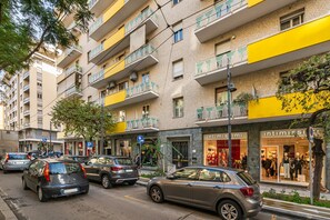 Un immeuble à plusieurs étages doté de balcons, une devanture de magasin avec des mannequins et des voitures garées dans la rue.