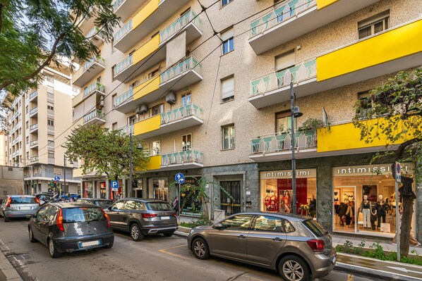 Un immeuble à plusieurs étages doté de balcons, une devanture de magasin avec des mannequins et des voitures garées dans la rue.