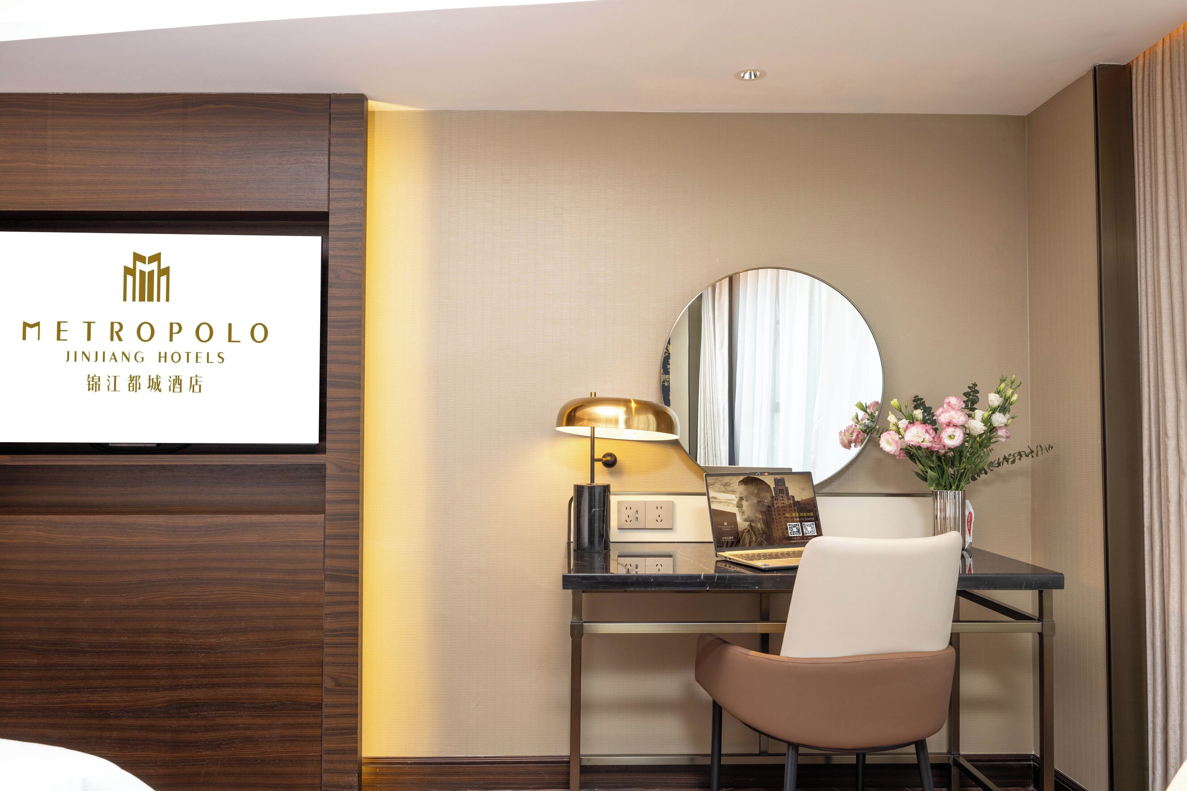 Habitación de hotel con escritorio, silla, lámpara, espejo y un cartel con la marca del hotel.
