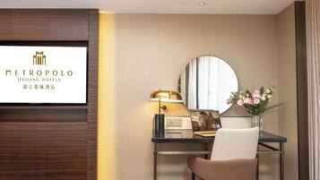 Habitación de hotel con escritorio, silla, lámpara, espejo y un cartel con la marca del hotel.