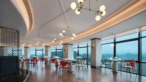 Un comedor moderno con varias mesas y sillas, amplias ventanas con vistas a la montaña e iluminación contemporánea.